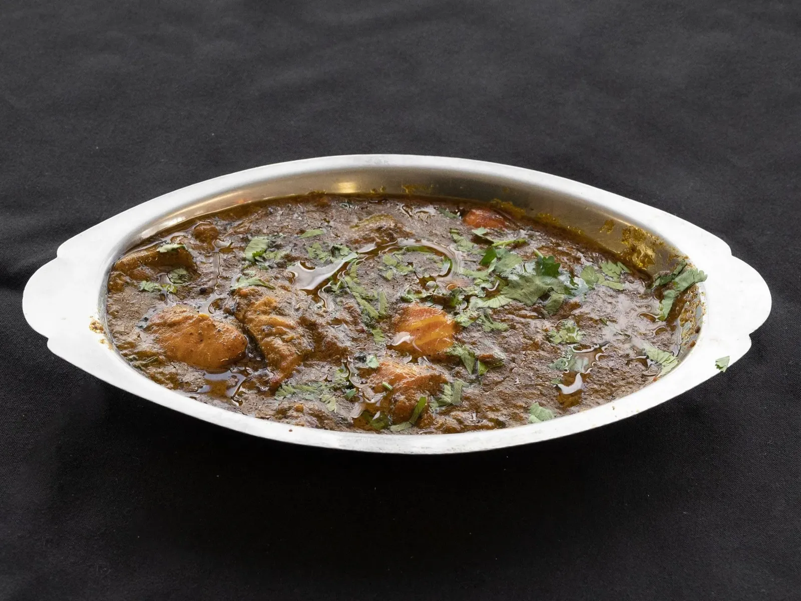 Chicken curry in a silver serving dish, garnished with fresh cilantro on a dark background.