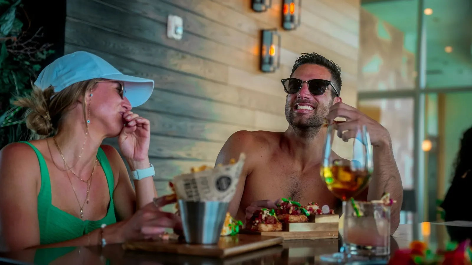 A man and woman are sitting at a table laughing and enjoying food and drinks at a restaurant or café.