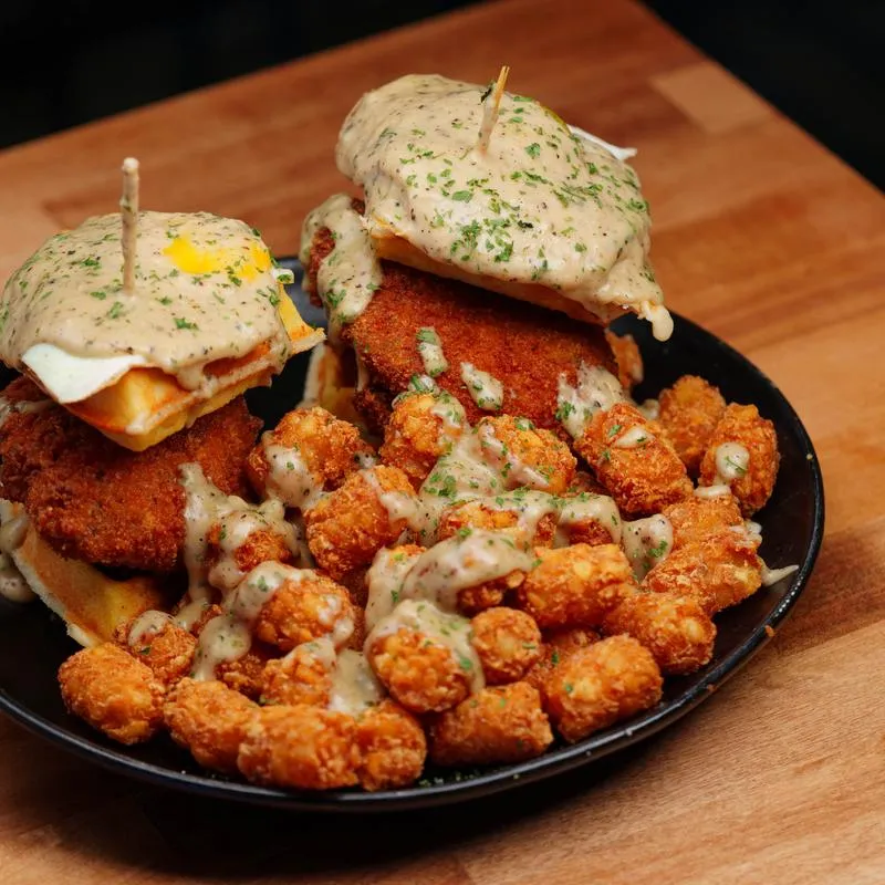 Chicken and waffle sandwich topped with fried eggs, gravy and served with tater tots.