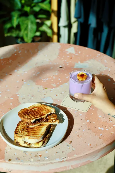 Grilled sandwich on plate next to purple drink with toasted marshmallow, terrazzo tabletop