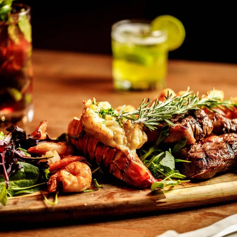 Grilled shrimp, lobster, and steak garnished with fresh rosemary, served on a wooden board.