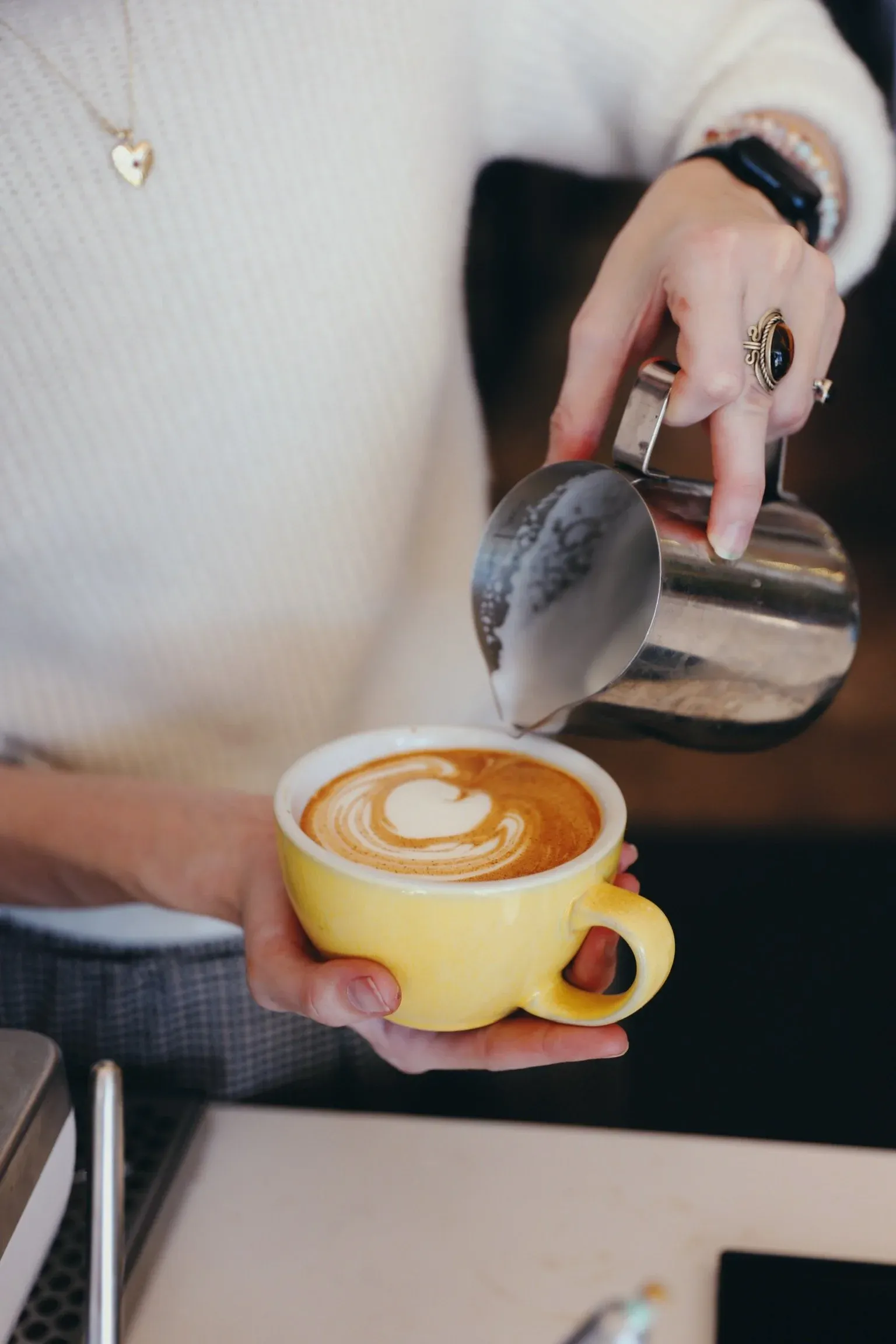 Person pouring latte art into yellow coffee cup