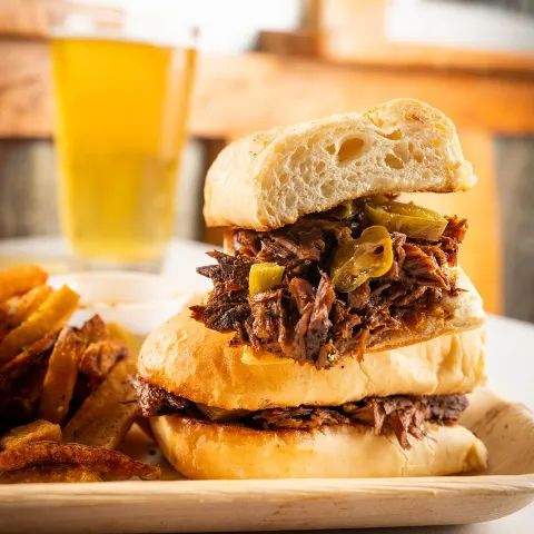 Pulled Pork Sandwich with fries, alongside glass of beer.
