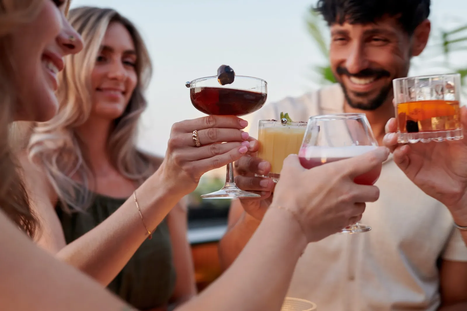 Group of friends raising colorful drinks in a toast at an outdoor gathering