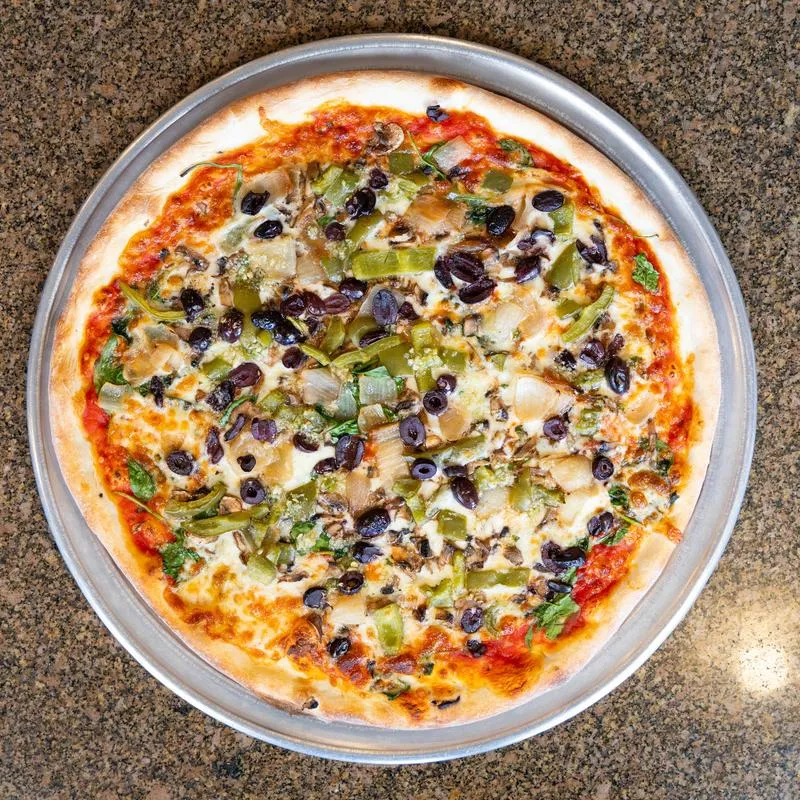 Vegetable pizza with olives and greens on a metal tray.