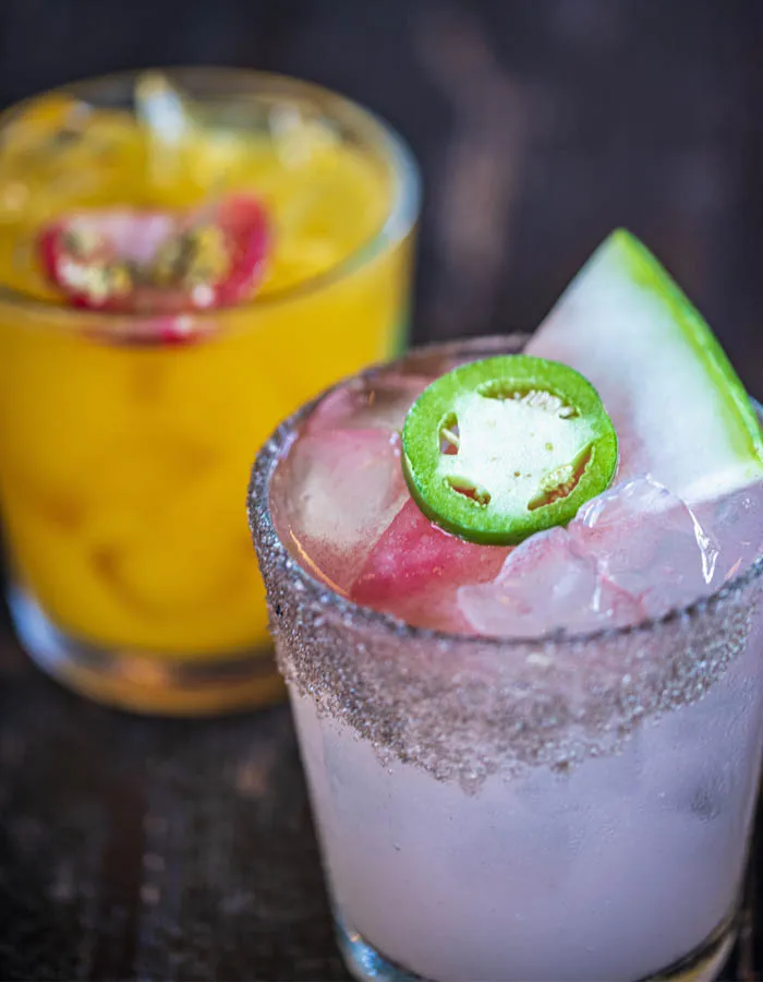 Two margaritas garnished with a jalapeño slice and watermelon wedge