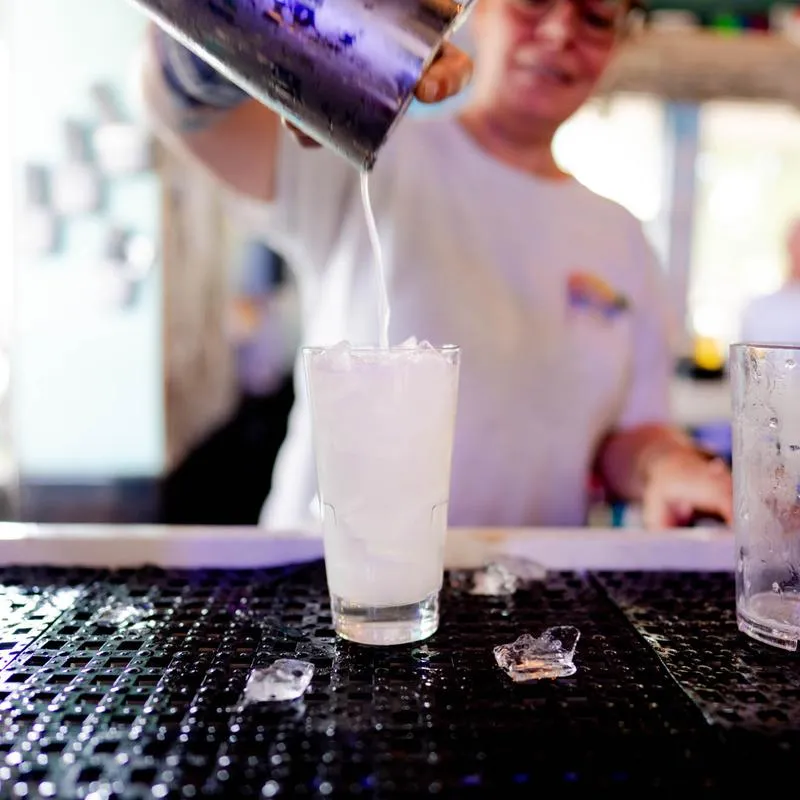 A bartender pouring a mixed drink into a glass on a bar counter mat.