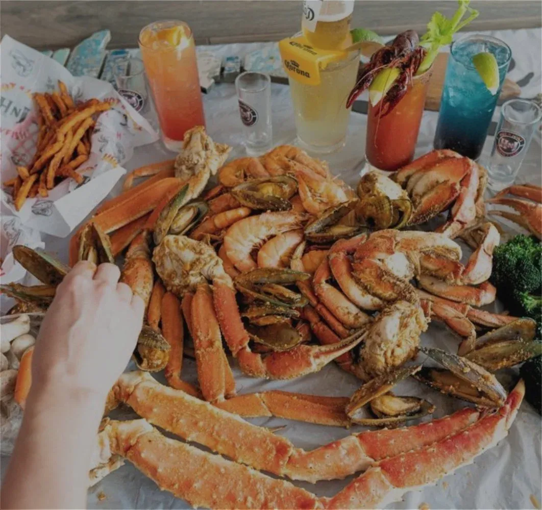 Seafood boil featuring crab legs, shellfish, cocktails, and beer served on a restaurant table.