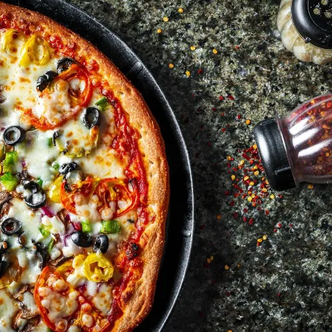 Meatless Delight pizza sits on a dark surface with shakers of seasonings.