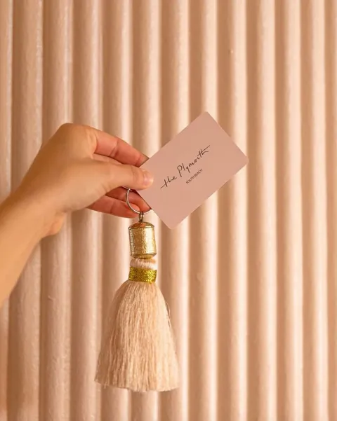 Hand holding the stylish, custom pink key card and tassel against a textured pink wall at The Plymouth Hotel South Beach