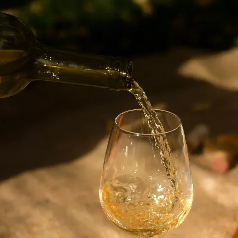 A glass of white wine being poured from a bottle.