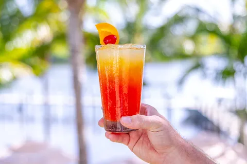 A hand holding a colorful layered cocktail with orange and red hues