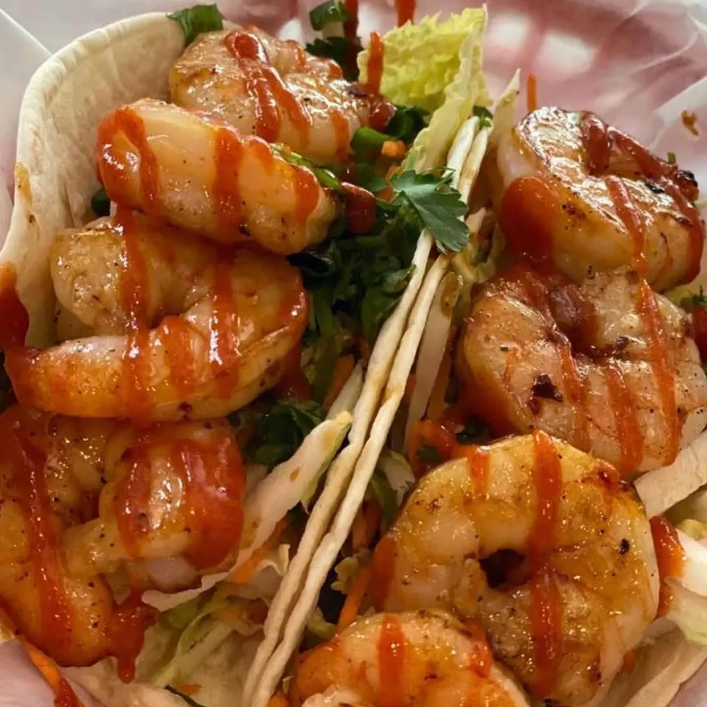 Two Shrimp Tacos topped with zesty sauce, fresh greens, and cilantro in soft tortillas, served in a basket.