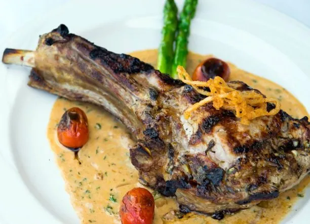 Grilled lamb chop served with creamy sauce, roasted cherry tomatoes, and asparagus