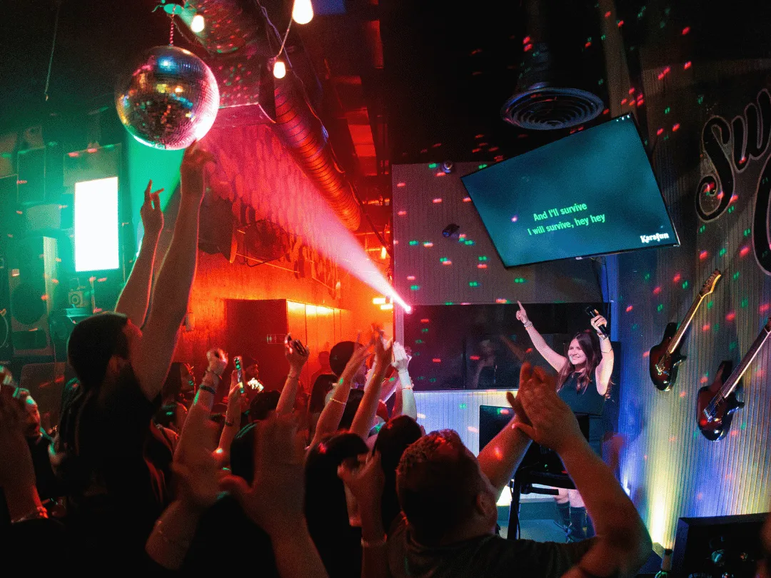 Group of people singing along to karaoke while the performer throws up her hands. Karaoke in Miami.