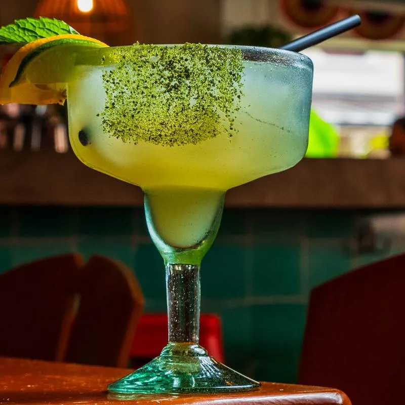 Margarita in stemmed glass with green rim and citrus garnish.