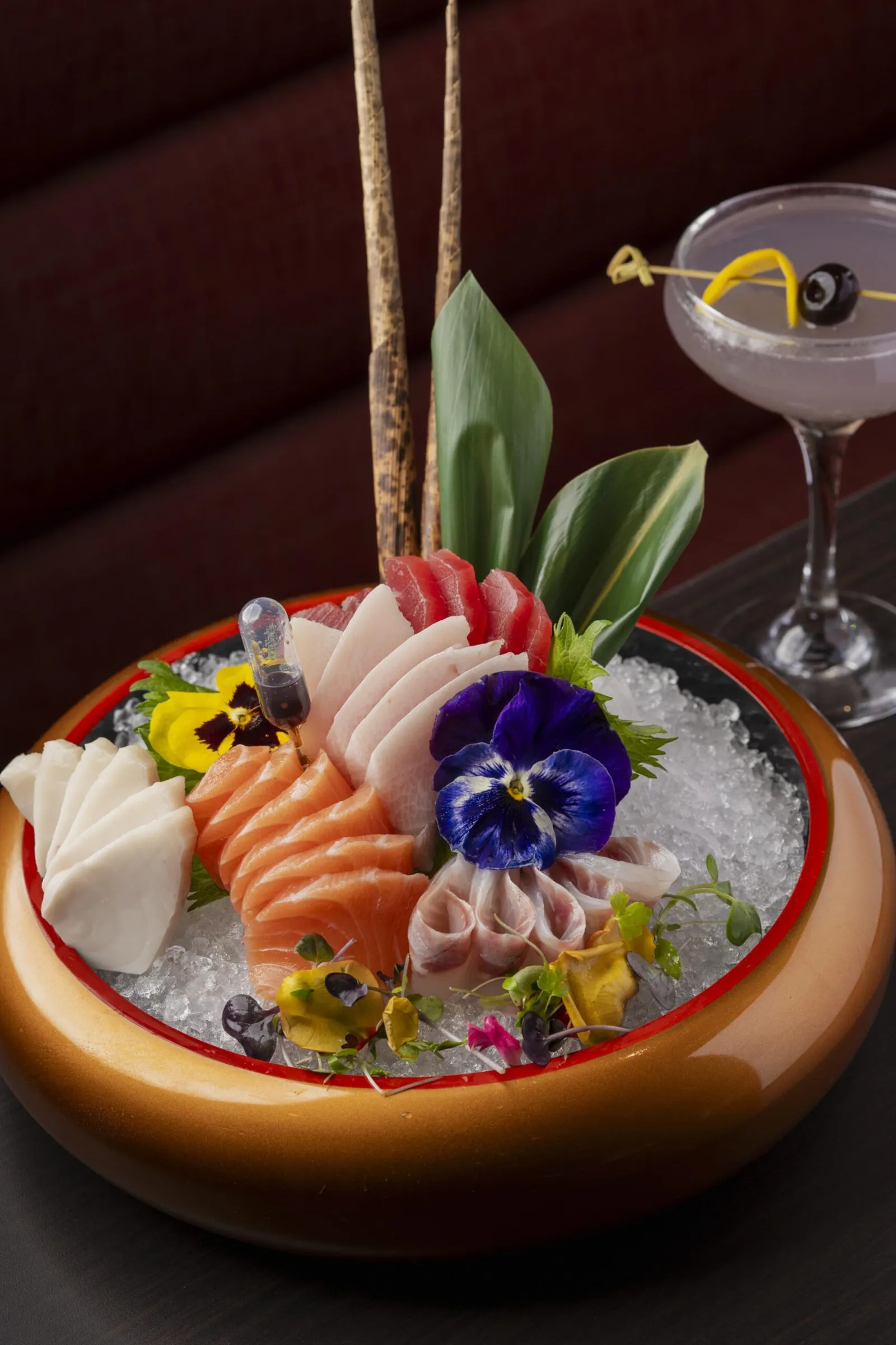 Assorted sashimi platter on ice with tuna, salmon, and white fish, garnished with edible flowers