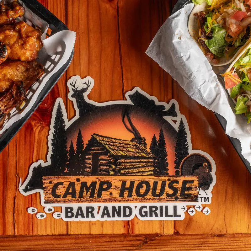 Camp House Bar and grill sign on a wooden table with food trays.