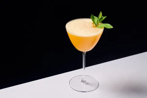 Elegant cocktail with orange liquid and mint garnish in a coupe glass on a black and white background.
