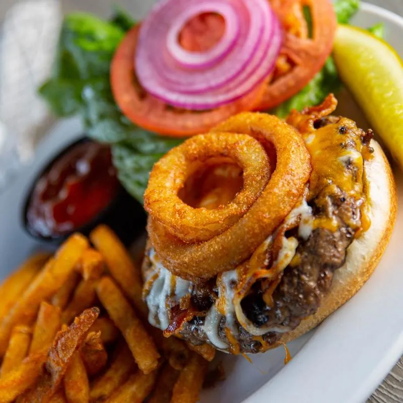 Burger with grilled meat, onion rings and salad, dip and fries on the side