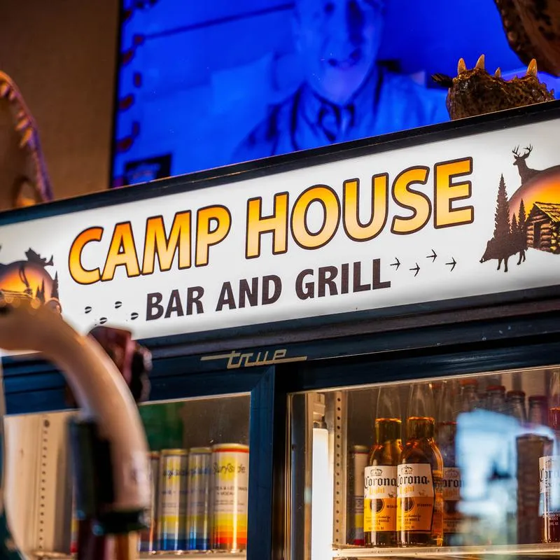 Illuminated Camp House bar sign above beverage coolers.