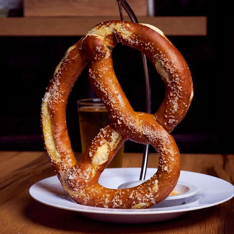 A  pretzel with a dip and a glass of beer.