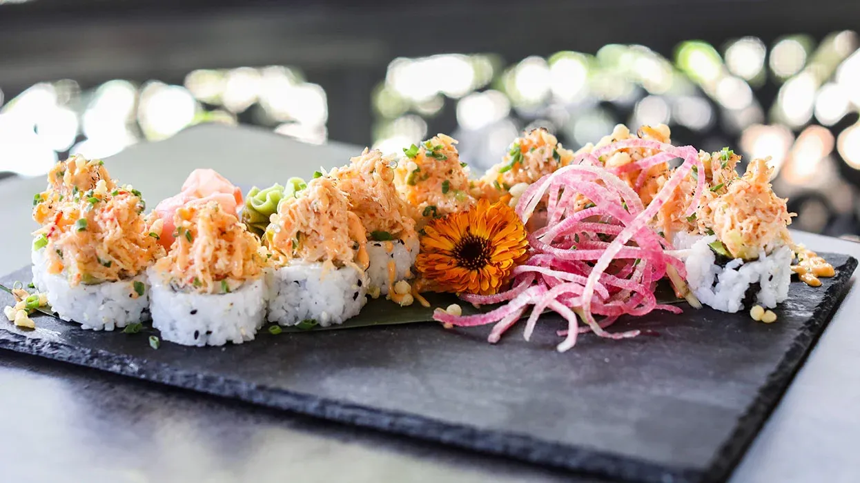 sushi roll at Magnolias on the Bay in Manasota Key displayed beautifully with a flower and pickled onion on a slate tray