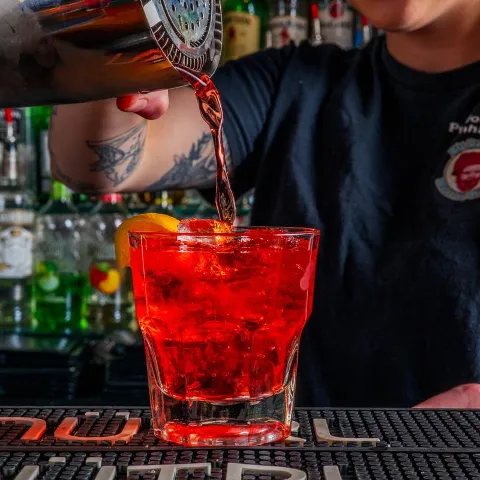 A bartender pouring red drink into a glass on bar counter.
