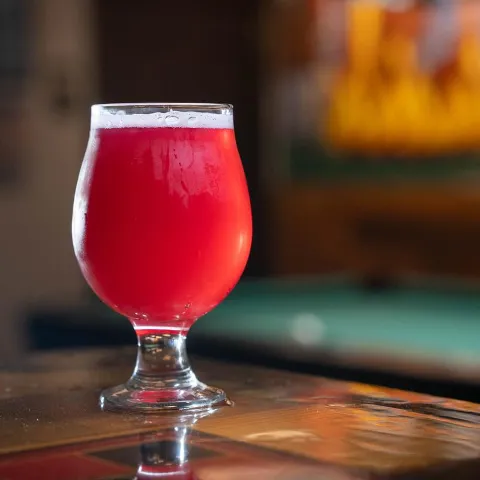 Pink craft beer in a tulip glass on a wooden counter.