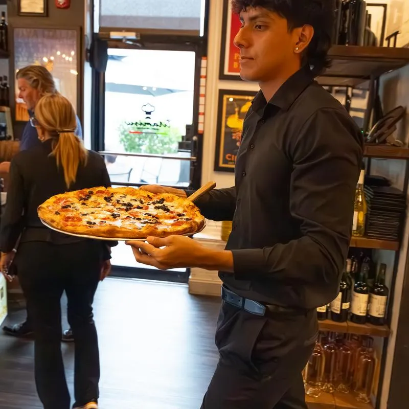 Served carrying a freshly baked pizza inside the restaurant.