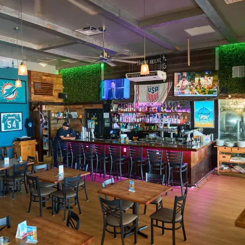 Interior featuring a long wooden bar counter with high stools and a seating area with tables.