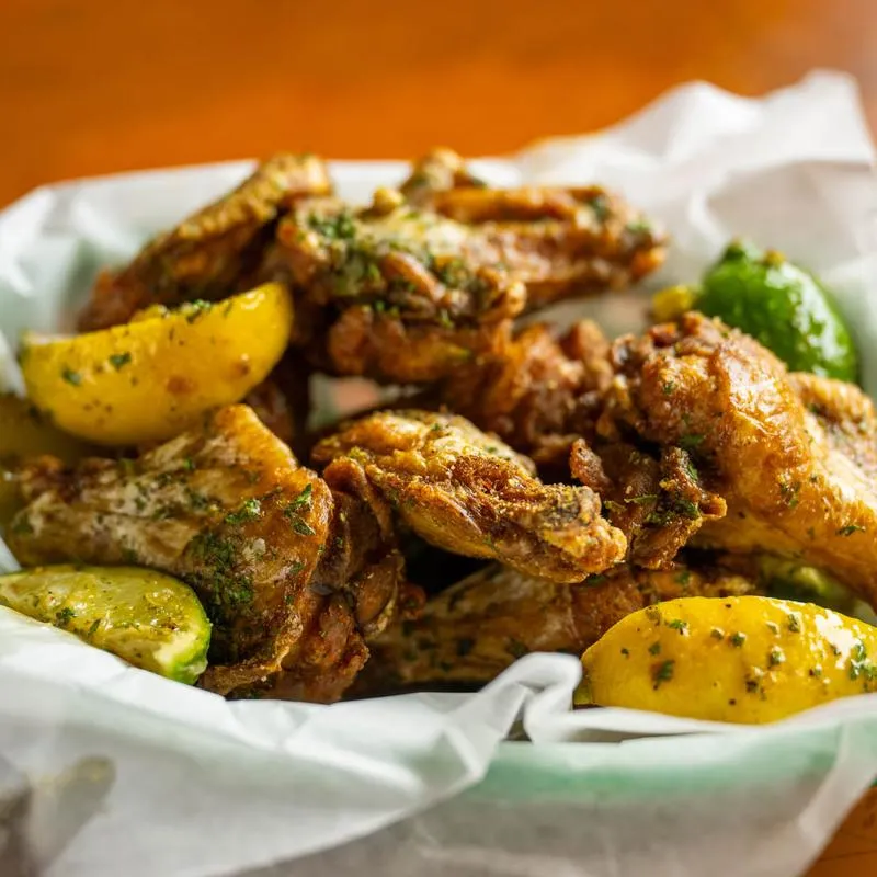 Seasoned chicken wings with lemon and lime wedges.
