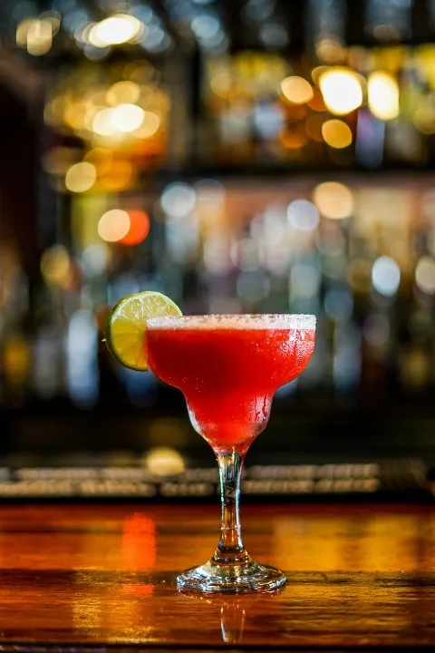 Red cocktail in a margarita glass with lime garnish on bar top