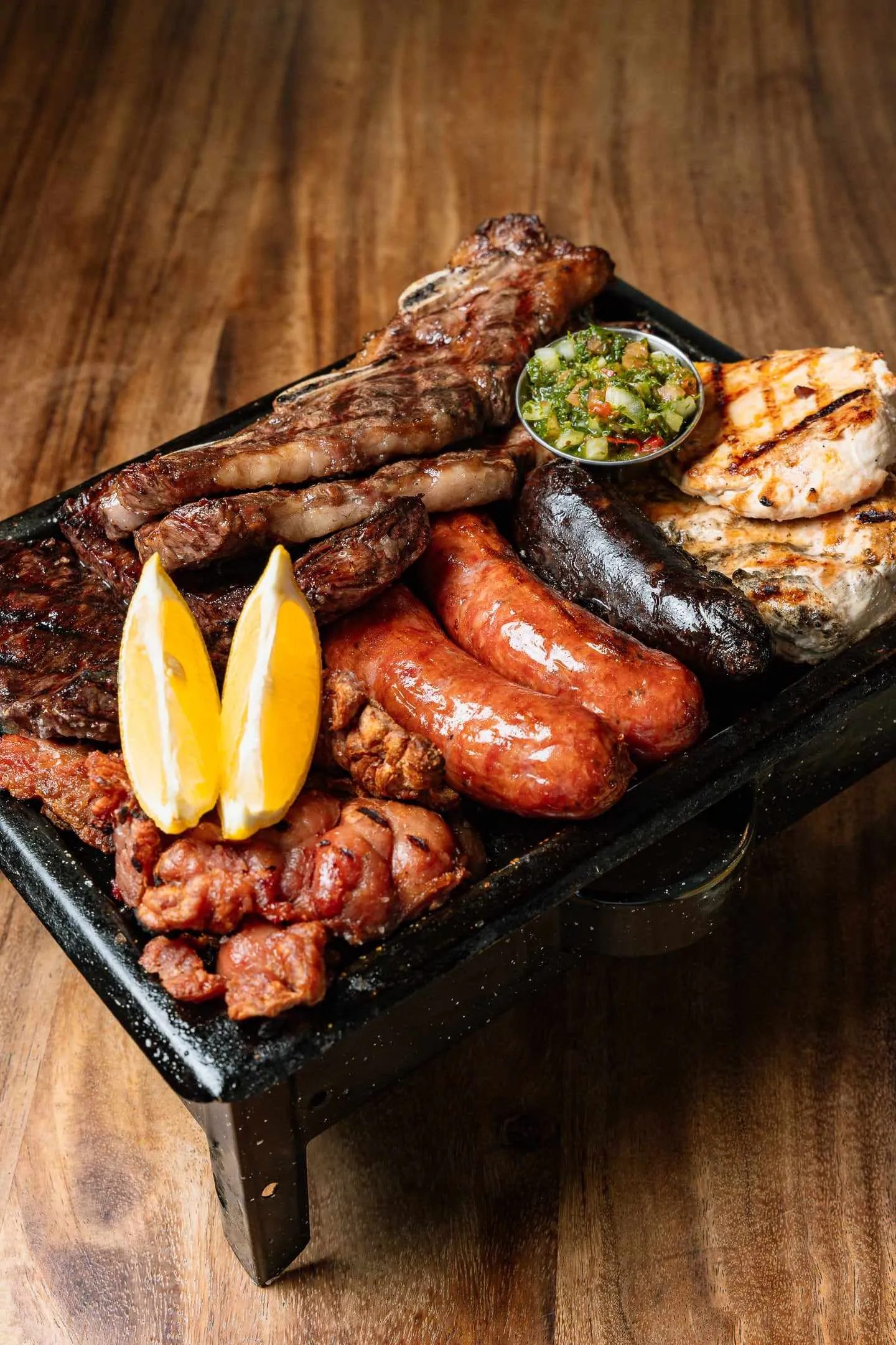 A parrillada on a tabletop brasero: chorizo, morcilla, skirt steak and half a lemon over the coals
