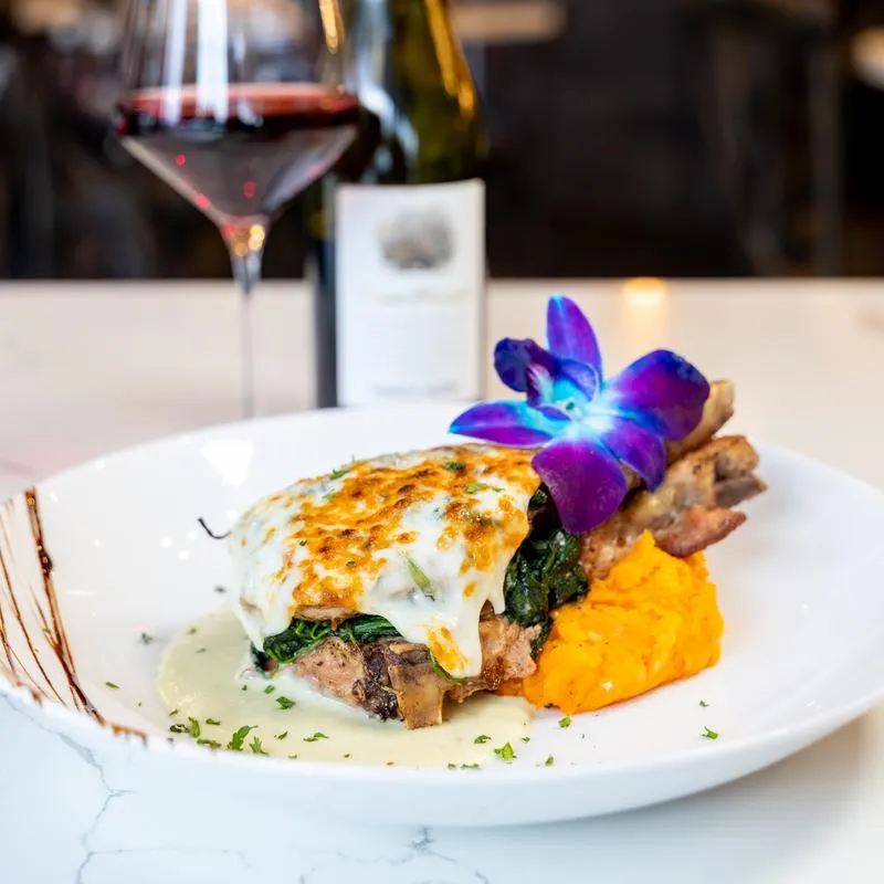 Pork chop with melted cheese and spinach, served with red wine.