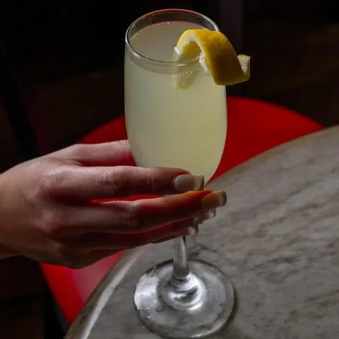 A person holding a glass with mimosa cocktail, garnished with lemon peel.