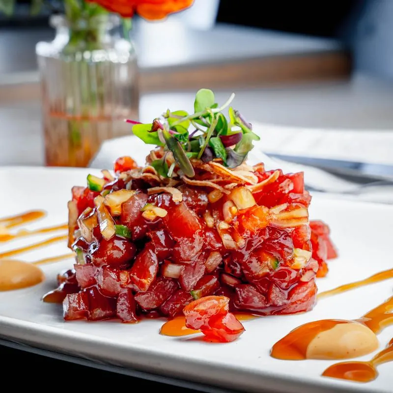 Ahi tuna tartare with herbs on a white plate.