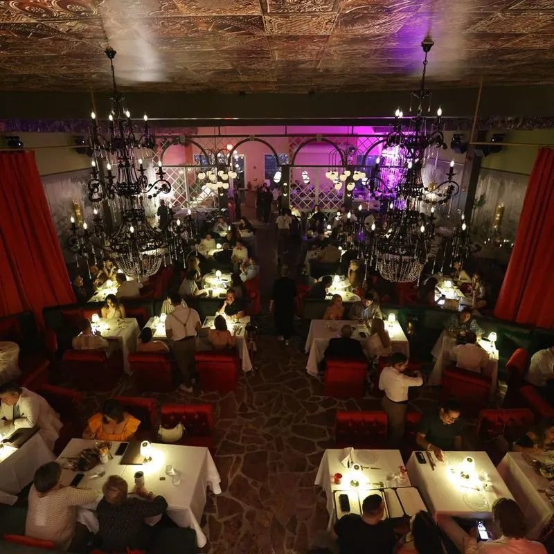 Crowded dining room with chandeliers and red curtains.