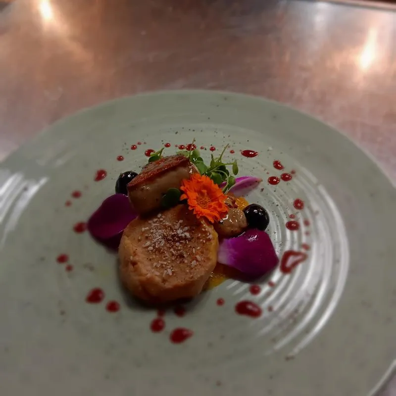 Fine dining dessert dish garnished with berries and flower petals.