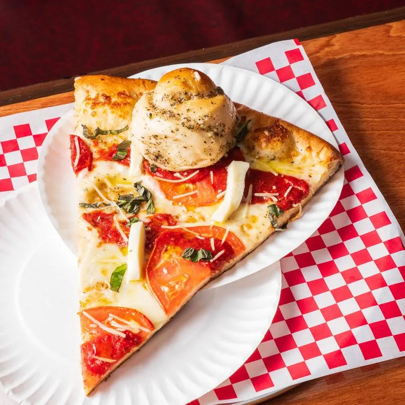 A slice of spinach tomato ricotta pizza served on a paper plate.