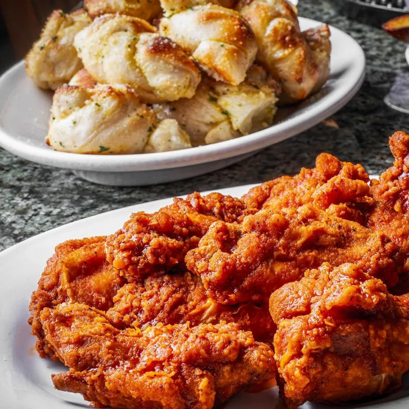Fried buffalo chicken wings on a plate with a plate of garlic bread knots in the background.
