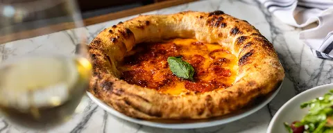 Image of a glass of wine with a pepperoni pizza with basil.