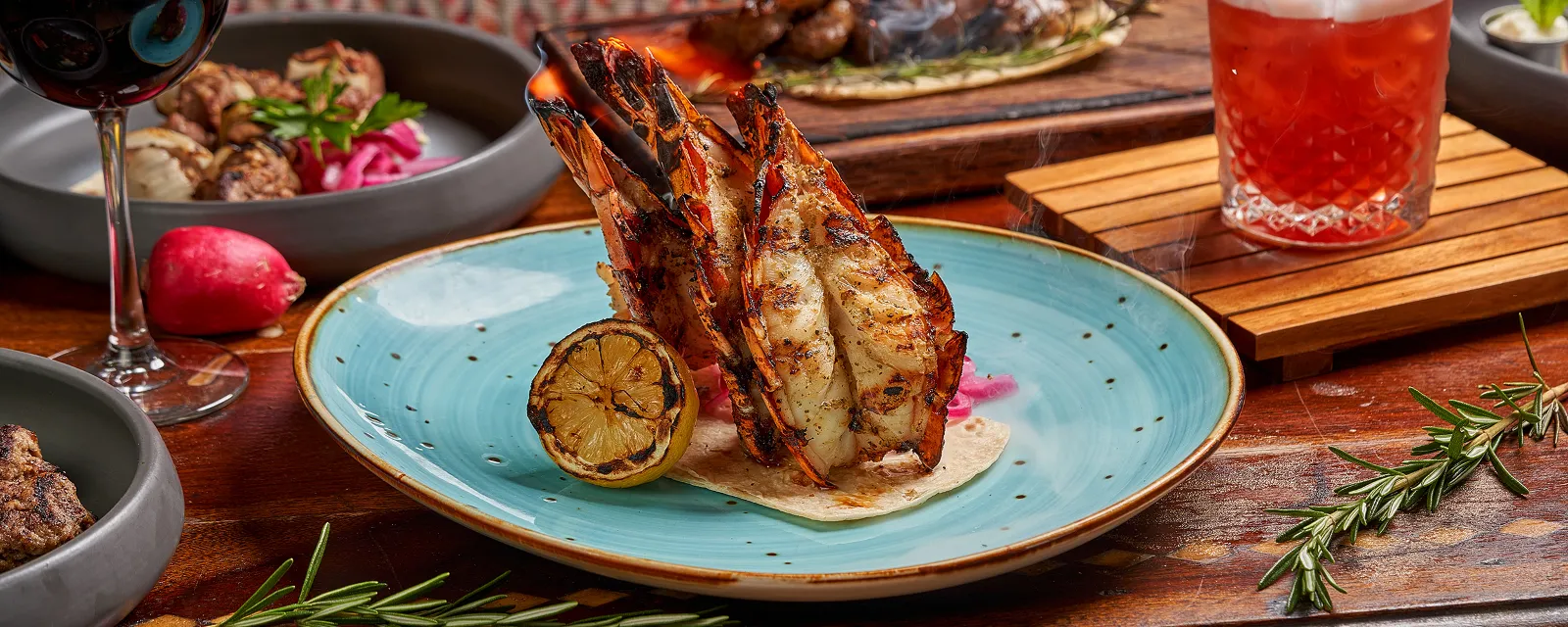 Grilled jumbo shrimp flambeed on a turquoise plate with charred lemon and pickled onions