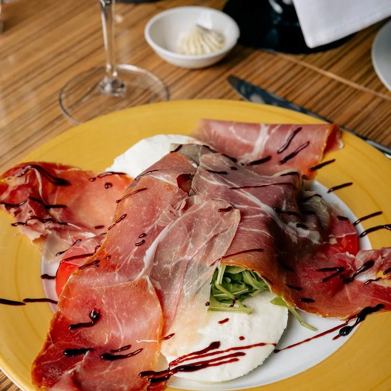 Veronica Caprese salad topped with prosciutto and balsamic glaze drizzle.