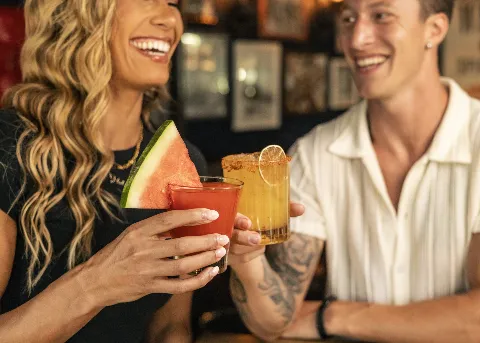 Two people toasting colorful cocktails at bar