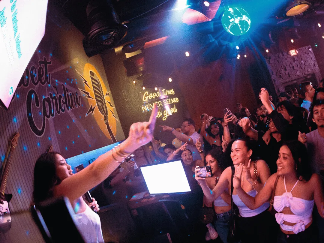 Saturday night karaoke party. Woman pointing at excited crowd as she sings karaoke.