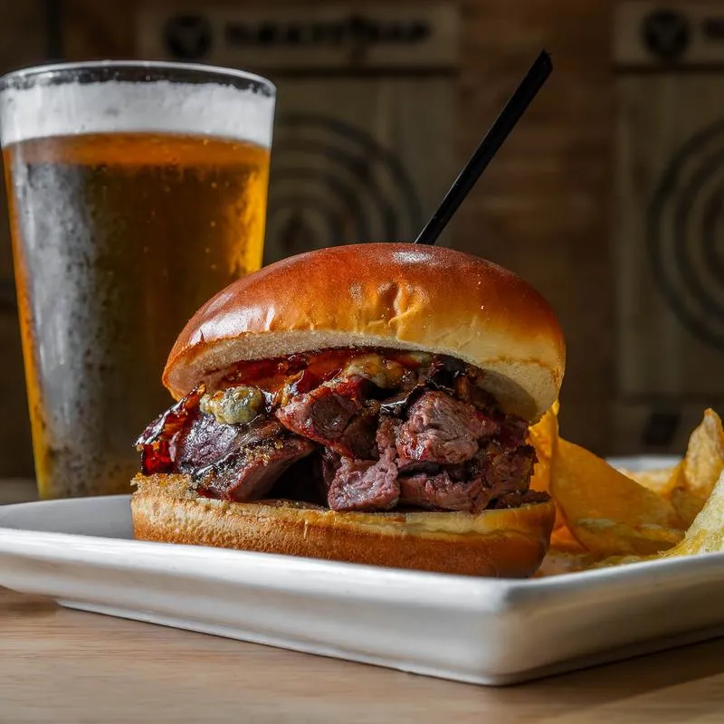 A steak sandwich with potato chips and a pint of beer on a table