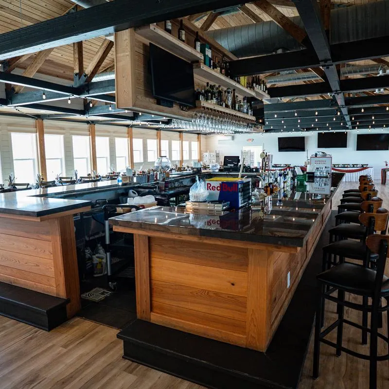 A modern interior - a central bar, high wooden beams and rows of tables by large windows.