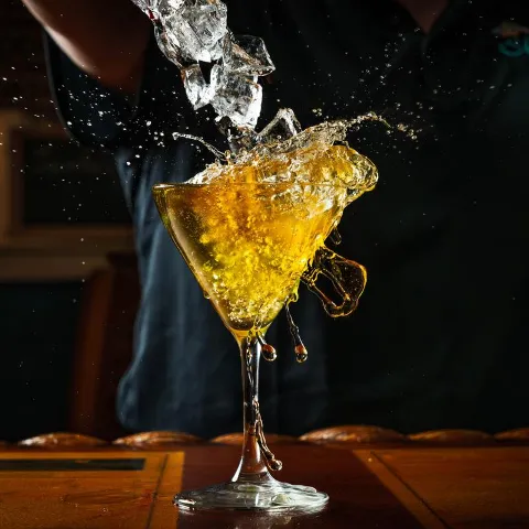 Ice cubes being dropped into martini glass with liquid splashing out.