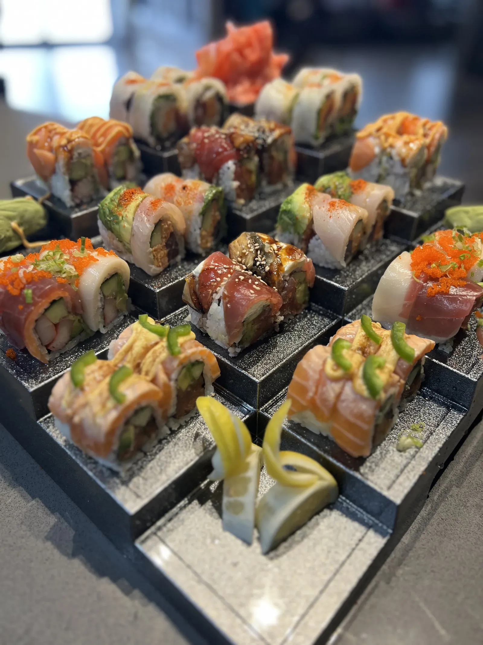 Assorted sushi rolls on a black display tray with pickled ginger and wasabi at the front.